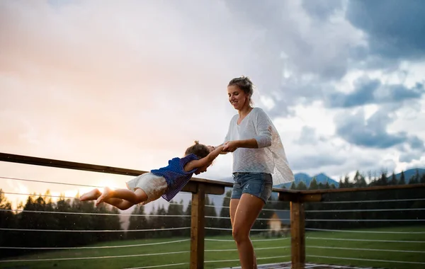 Mutter mit kleiner Tochter spielt auf der Terrasse der Holzhütte, Urlaub in der Natur. — Stockfoto