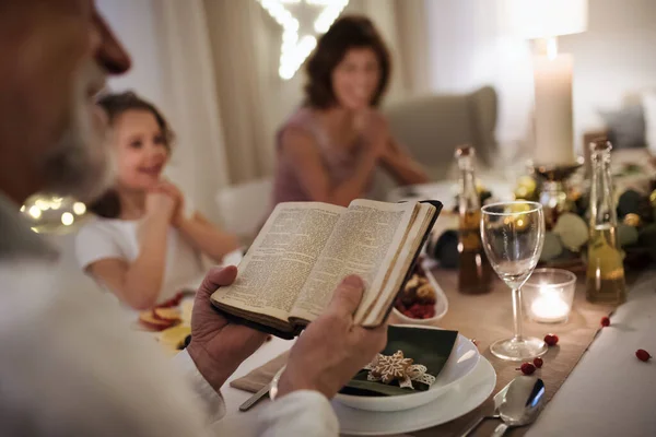 Mała dziewczynka z dziadkami siedzącymi w domu i świętującymi Boże Narodzenie, czytającymi Biblię. — Zdjęcie stockowe