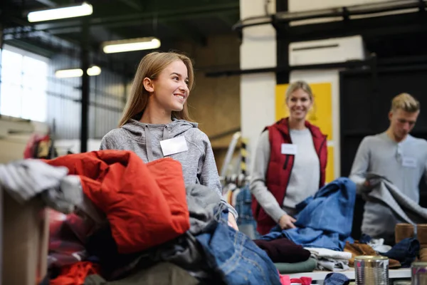 Voluntários ordenando roupas doadas em centro de doação de caridade comunitária. — Fotografia de Stock
