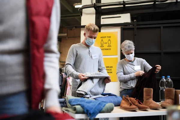 Voluntários ordenando roupas doadas no centro de doação de caridade comunitária, conceito de coronavírus. — Fotografia de Stock