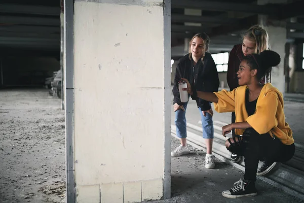 Grupo de adolescentes gangue dentro de casa em prédio abandonado, usando tinta spray na parede. — Fotografia de Stock