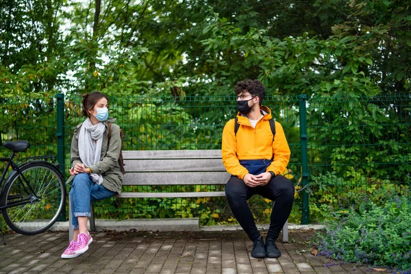 Jóvenes hablando en el banco al aire libre en la ciudad. Coronavirus y concepto de distancia segura. — Foto de Stock