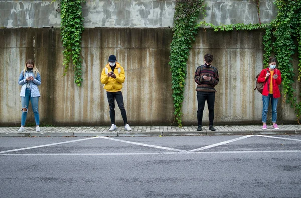 Giovani che usano smartphone all'aperto in città. Coronavirus e concetto di distanza di sicurezza. — Foto Stock