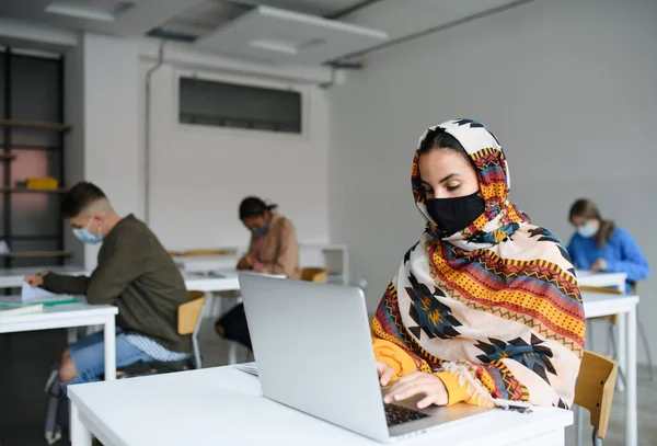 Islamitische student met gezichtsmasker aan de balie van universiteit of universiteit, coronavirus concept. — Stockfoto