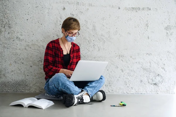 Ung student med bärbar dator sitter på golvet tillbaka på college eller universitet, coronavirus koncept. — Stockfoto