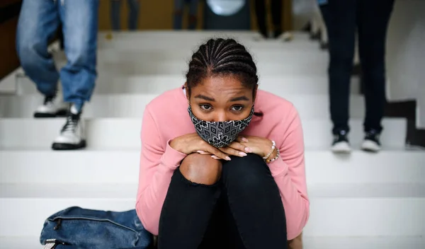 Giovane studente depresso con maschera facciale seduto sul pavimento di nuovo al college o all'università, concetto coronavirus. — Foto Stock