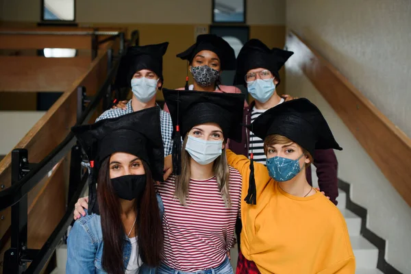 Jovens estudantes com máscaras faciais e bonés de graduação de volta na faculdade ou universidade, conceito coronavírus. — Fotografia de Stock