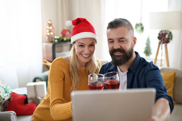 Gelukkig paar met wijn binnen in huis met Kerstmis, met video bellen met familie. — Stockfoto