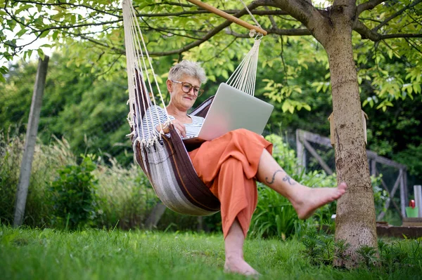 Портрет активної старшої жінки з ноутбуком, що працює на відкритому повітрі в саду, концепція домашнього офісу . — стокове фото