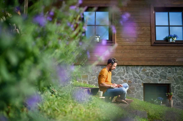 Gammal man med bärbar dator arbetar utomhus i trädgården, hemmakontor koncept. — Stockfoto