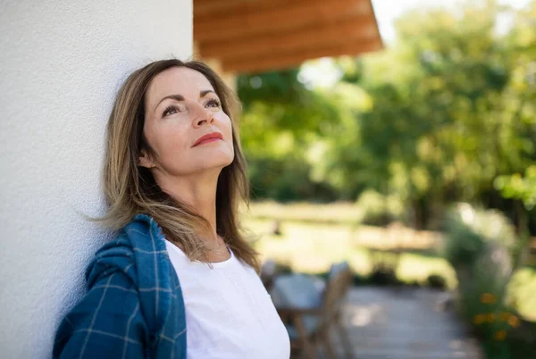 Volwassen vrouw rustend buiten, leunend op muur van huis. — Stockfoto