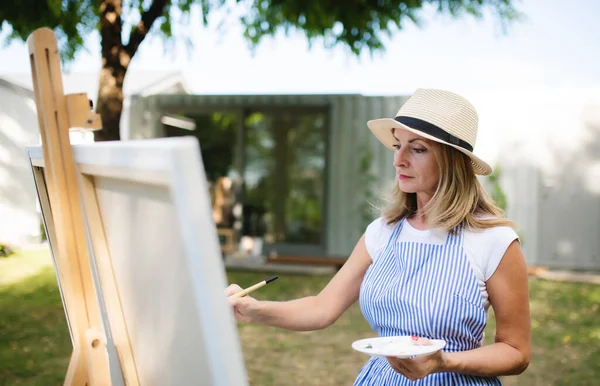 Portrait of mature woman with pallete painting outdoors in garden. — Stock Photo, Image