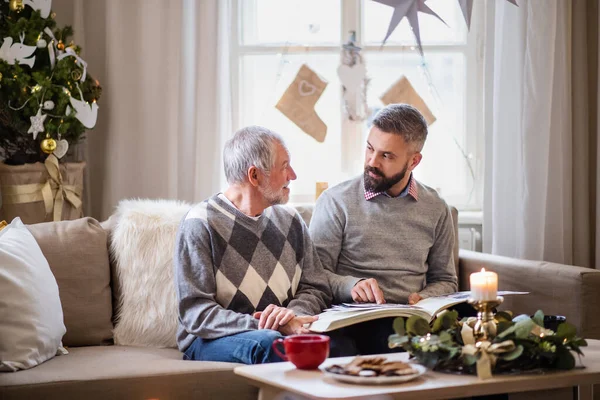 Homme mûr et père aîné à l'intérieur à la maison à Noël, en regardant les phootgraphes. — Photo