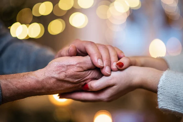 Hand eines älteren Mannes hält Hand einer jungen Frau zu Weihnachten drinnen, Nahaufnahme. — Stockfoto