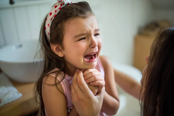 Llorando niña pequeña con madre irreconocible en el interior, perdiendo diente de bebé. — Foto de Stock