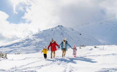 Anne ve baba kışın iki küçük çocukla karda yürüyorlar..