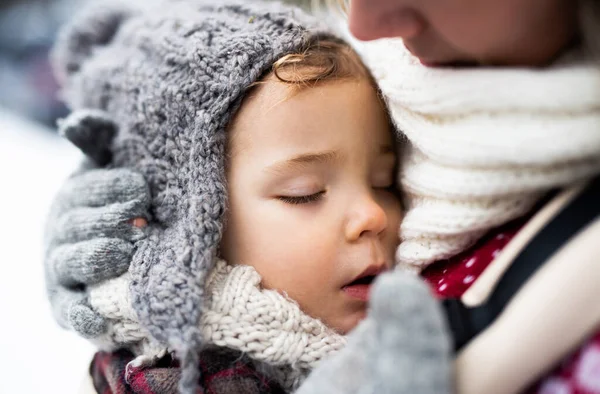 Närbild av sovande liten dotter i bärare och mor i vinter natur. — Stockfoto