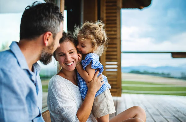 Famiglia con piccola figlia seduta sul patio della cabina in legno, concetto di vacanza nella natura. — Foto Stock