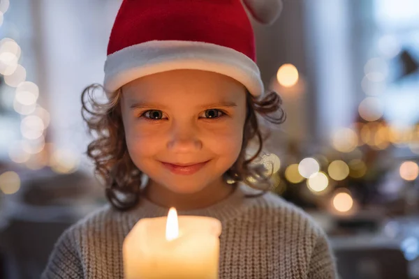 Wesoła mała dziewczynka z kapeluszem Mikołaja wewnątrz w Boże Narodzenie, trzymając świecę. — Zdjęcie stockowe