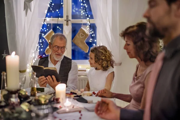 Senior man with extended family indoors celebrating Christmas, reading Bible. — Stock Photo, Image