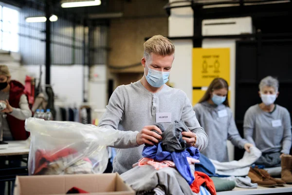 Volontärer sortera ut donerade kläder i samhället välgörenhet donationscenter, coronavirus koncept. — Stockfoto