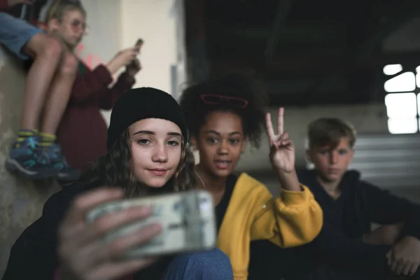 Grupo de adolescentes gangue sentado dentro de casa em prédio abandonado, tirando selfie com smartphone. — Fotografia de Stock