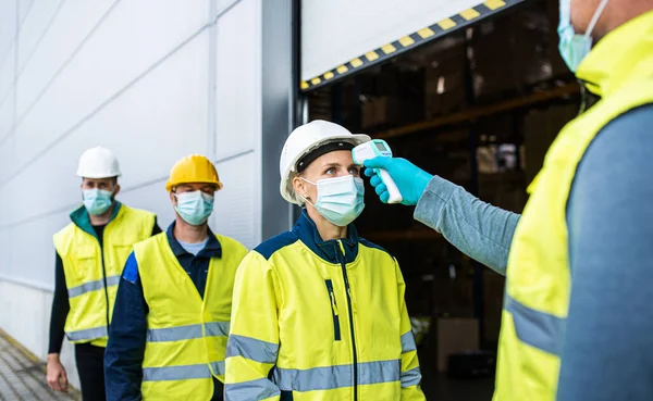 Grupo de trabajadores con mascarilla facial frente a almacén, coronavirus y concepto de medición de temperatura. — Foto de Stock