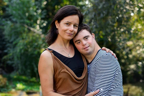 Portrait of down syndrome adult man with mother standing outdoors in garden. — Stock Photo, Image