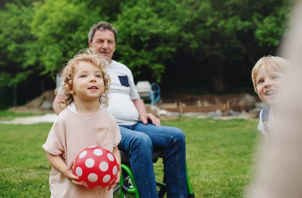 Kleine kinderen met oudere grootouders in een rolstoel die spelen. — Stockfoto