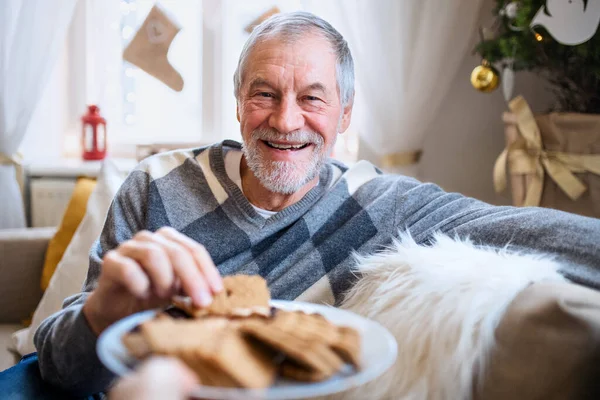 Ritratto di uomo anziano in casa a Natale, mangiare biscotti. — Foto Stock