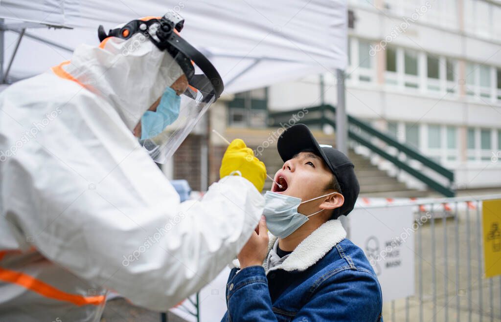 Young man in covid-19 testing center outdoors on street, coronavirus and taking swab concept.