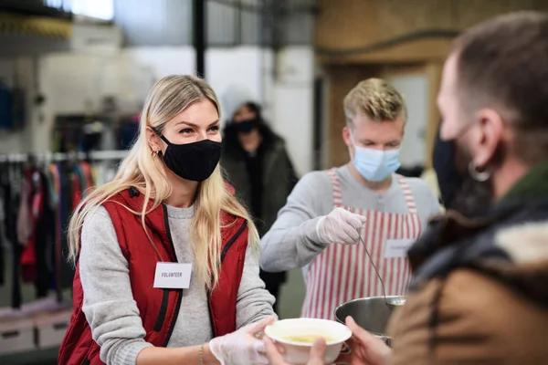 Önkéntesek forró levest szolgálnak fel hajléktalanoknak a közösségi jótékonysági adományozó központban, a koronavírus koncepciója. — Stock Fotó