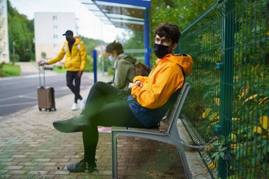 Şehirdeki otobüs durağında oturan genç adam. Coronavirus konsepti.