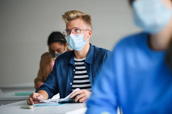 Молодые студенты в масках за партами в колледже или университете, концепция коронавируса. — стоковое фото