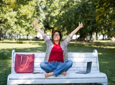 Şehir veya şehir parkında dizüstü bilgisayarı olan olgun bir kadın dinleniyor..