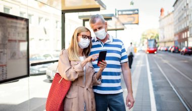 Şehirdeki ya da kasabadaki otobüs duraklarında akıllı telefonları olan yaşlı bir çift. Coronavirus konsepti..