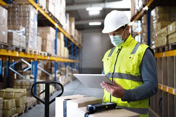 Hombre trabajador con tableta trabajando en interiores en almacén, concepto coronavirus. — Foto de Stock