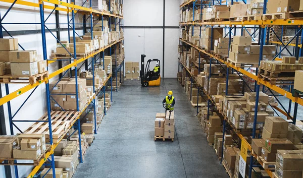 Pria bekerja dengan forklift dan pallet truk bekerja di dalam ruangan di gudang, konsep coronavirus. — Stok Foto