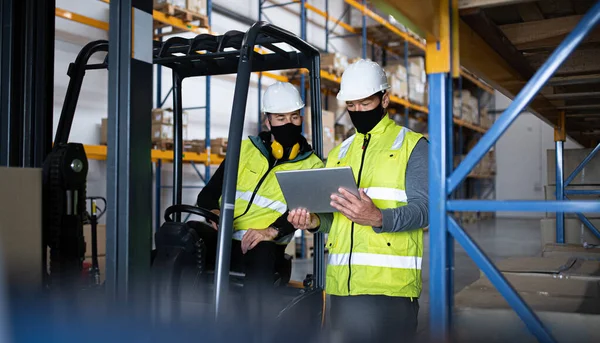 Arbeiter mit Mundschutz und Tablette arbeiten drinnen im Lager, Coronavirus-Konzept. — Stockfoto