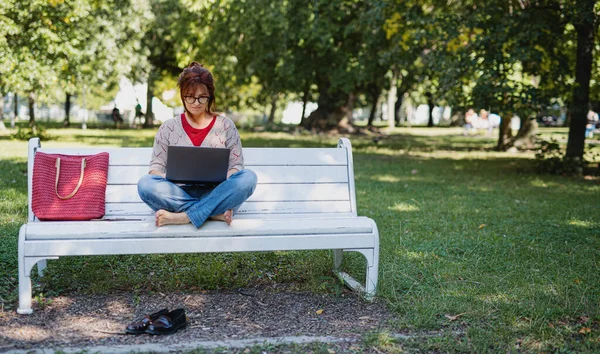 Gammal kvinna med bärbar dator utomhus i staden eller stadsparken, arbetar. — Stockfoto