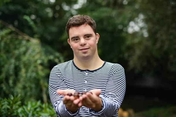 Porträt eines erwachsenen Mannes mit Down-Syndrom, der vor grünem Hintergrund im Freien steht und Nüsse hält. — Stockfoto