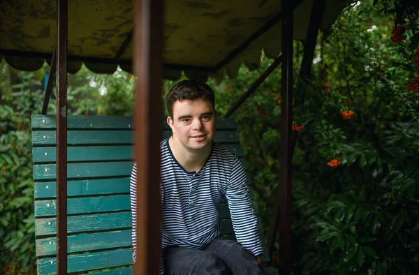 Portrait of down syndrome adult man sitting outdoors in garden, looking at camera. — Stock Photo, Image