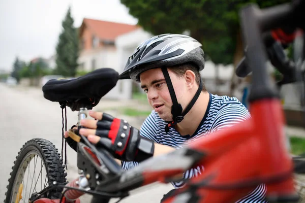 Porträtt av down syndrom vuxen man med cykel står utomhus på gatan, reparera. — Stockfoto