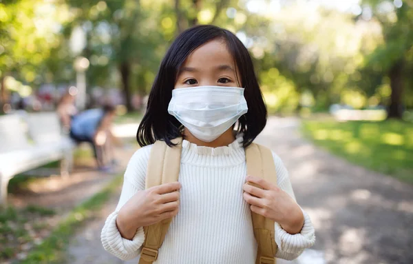 코로나 바이러스 개념의 조그만 일본 소녀 가방을 들고 마을 밖에서 있는 모습. — 스톡 사진