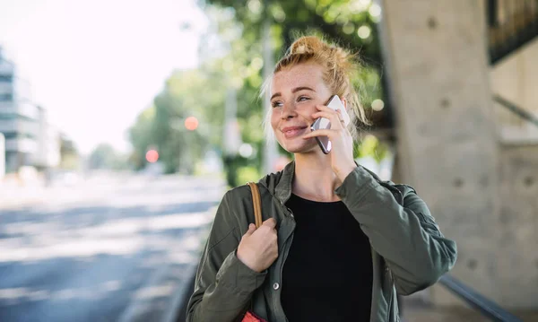 Ritratto di giovane donna allegra con i capelli rossi all'aperto in città, utilizzando lo smartphone. — Foto Stock