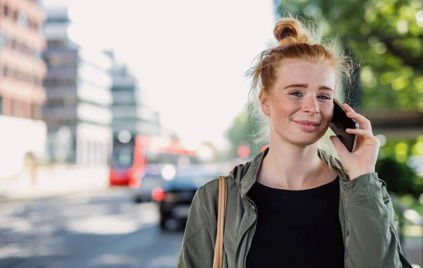 Kasabada açık havada kızıl saçlı, akıllı telefon kullanan neşeli genç bir kadının portresi.. — Stok fotoğraf