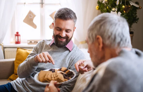 Ώριμος άντρας και πατέρας σε εσωτερικούς χώρους στο σπίτι τα Χριστούγεννα, τρώγοντας μπισκότα. — Φωτογραφία Αρχείου
