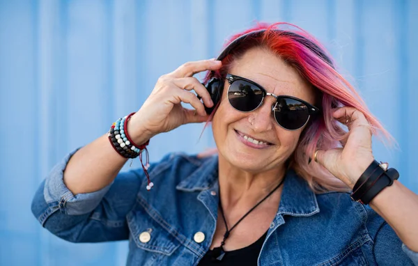 Senior woman with purple pink hair and sunglasses standing against blue background. — Stock Photo, Image
