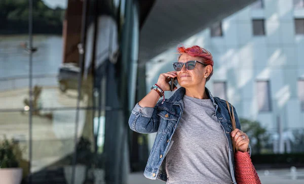 Senior kvinna med lila rosa hår och smartphone promenader utomhus i stad eller stad. — Stockfoto