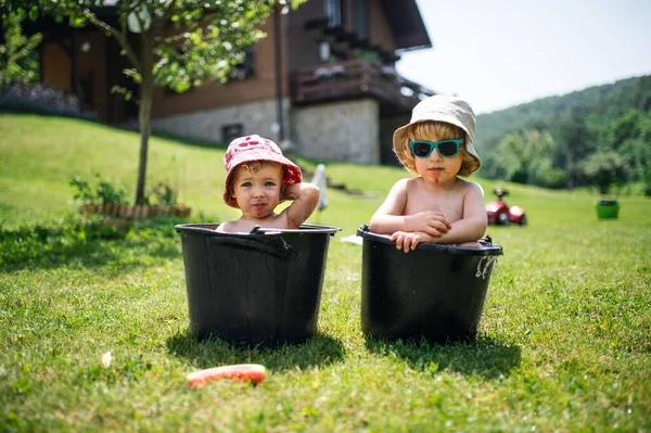 Topless kleine jongen en meisje met hoeden in emmers buiten in de zomer tuin. — Stockfoto